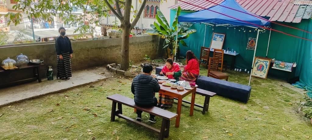 Guests eating at a wooden table on the backyard lawn beside a banana plant and a small tent